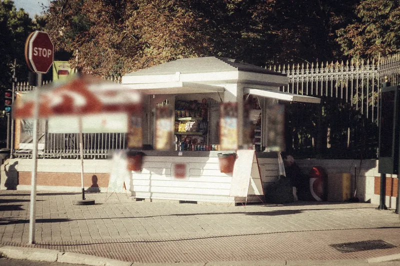 Quiosco de estilo retro en una acera soleada de Madrid, con una sombrilla roja y una señal de stop a su lado.